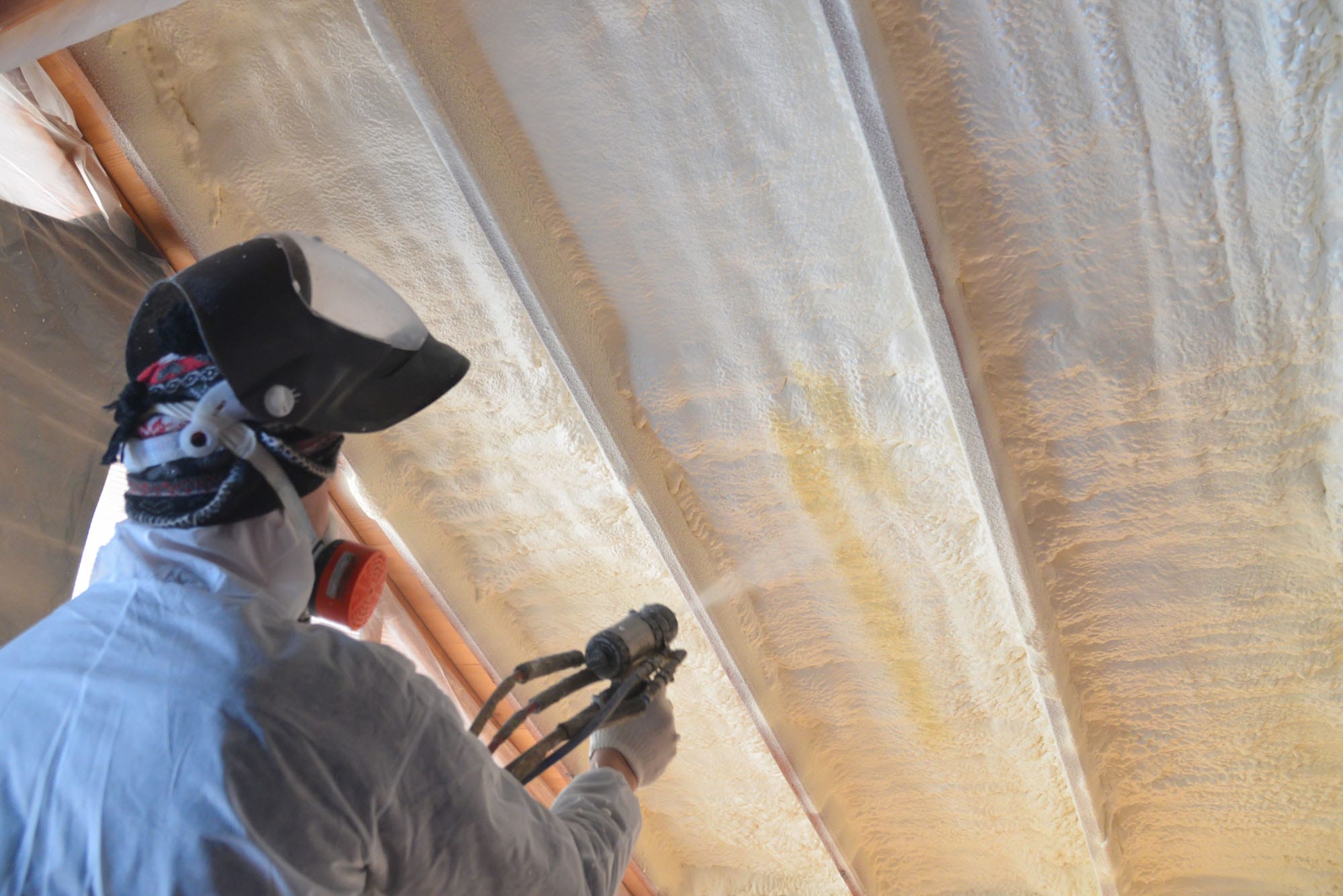 Worker applying spray foam insulation to ceiling.