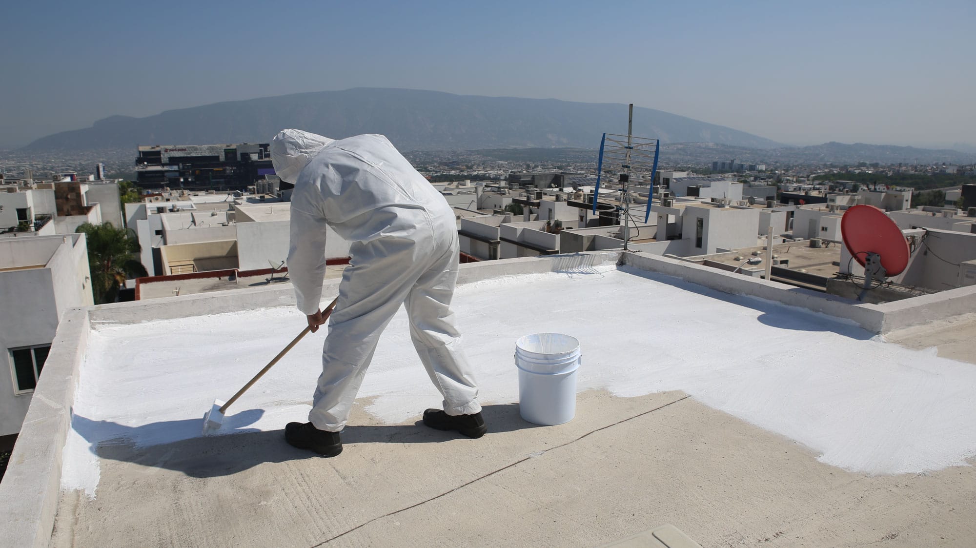 Person in suit painting rooftop white in urban area.
