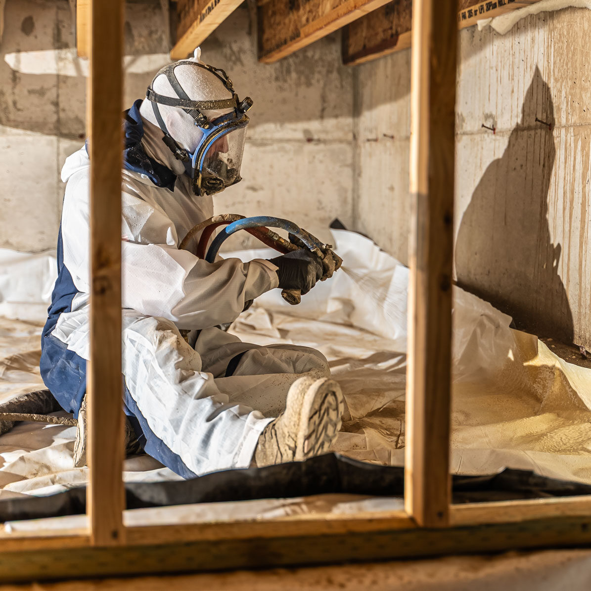 Worker applying insulation in a crawl space.