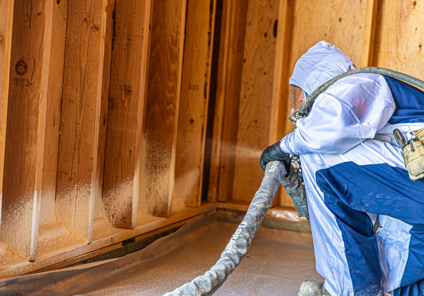 Worker applying spray foam insulation to wooden wall.