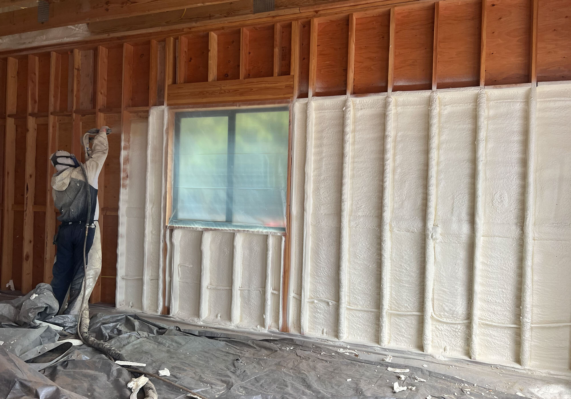 Worker spraying foam insulation on wooden wall.