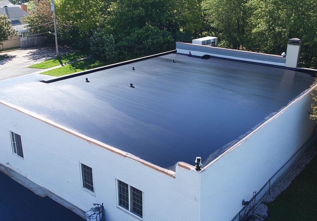 Flat black roof on white building with trees nearby.