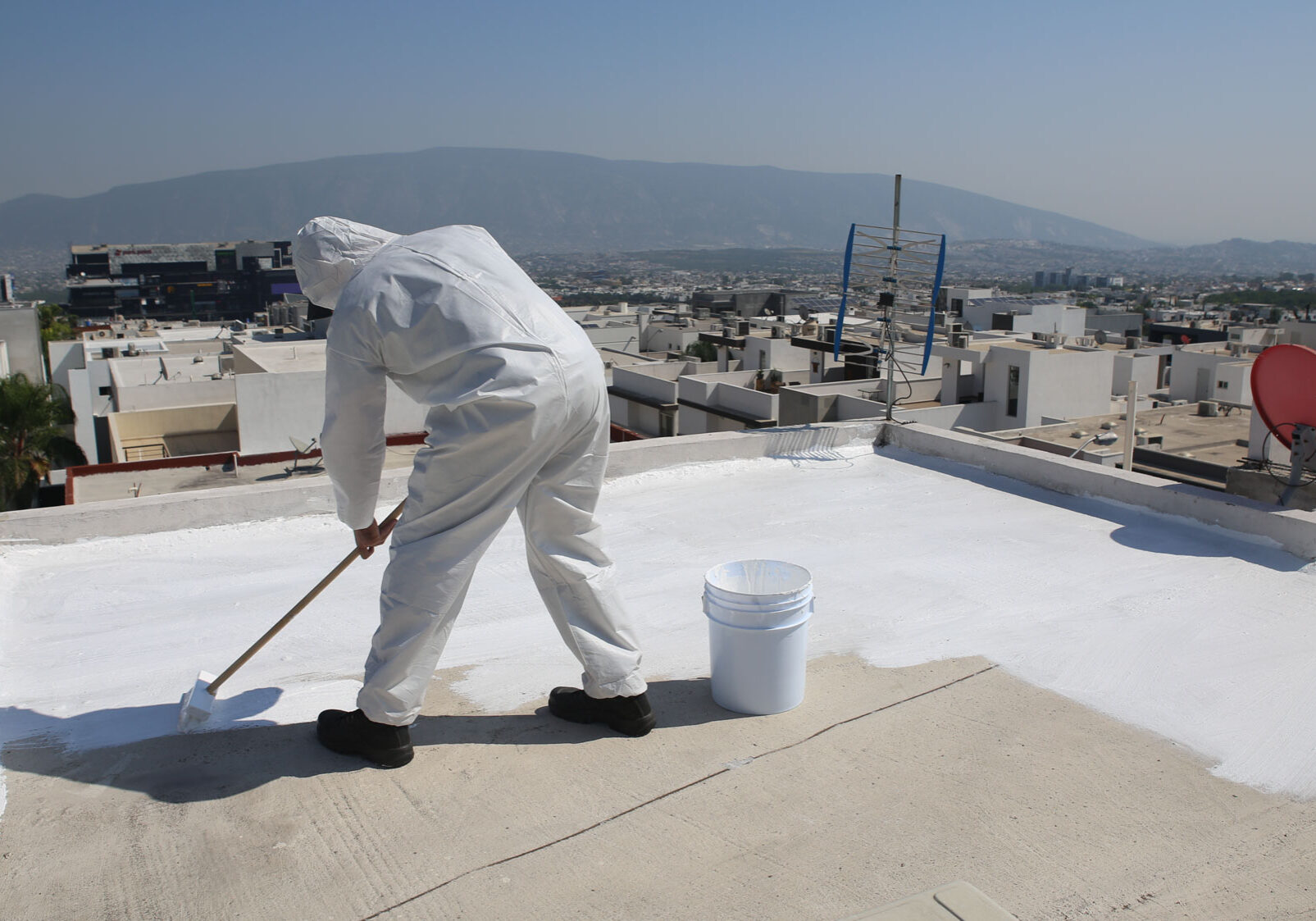 AdobeStock_301433947 Person in suit painting rooftop white in urban area.
