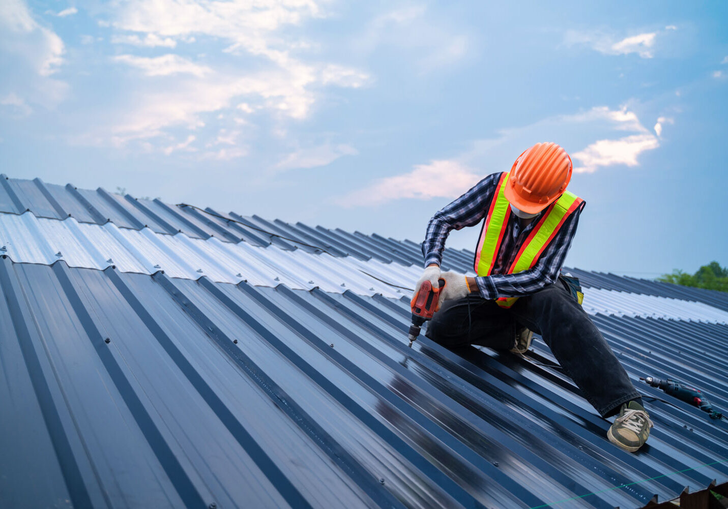 Asian Roofer worker safety wear using air or pneumatic nail gun Worker drilling on metal roof, wearing safety gear.